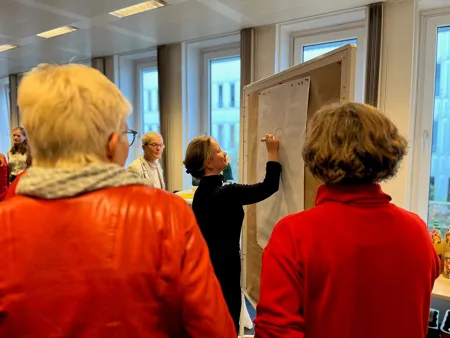 Eine Teilnehmerin schreibt an eine Metaplanwand. Weitere Teilnehmende stehen drumherum.