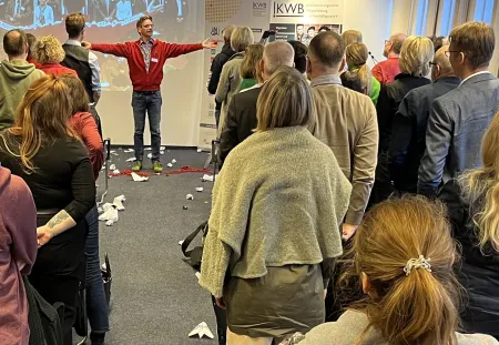 Gaedt steht mit ausgebreiteten Armen vor dem Publikum. Am Boden liegen Papierbälle und -flieger.