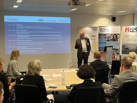 Dr. Martin Makait steht vor dem Publikum, hinter ihm die Leinwand mit der Agenda, vor ihm das Publikum